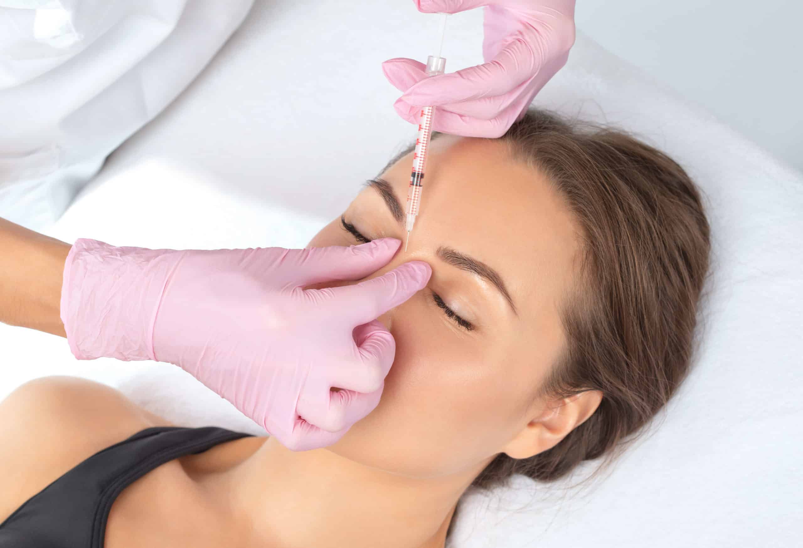 Young asian woman closing her eyes in pain while getting prick of botox injection in her brow area. Girl is frowning her forehead for Frown Lines | Bellava Aesthetics in Crestview Hills, KY